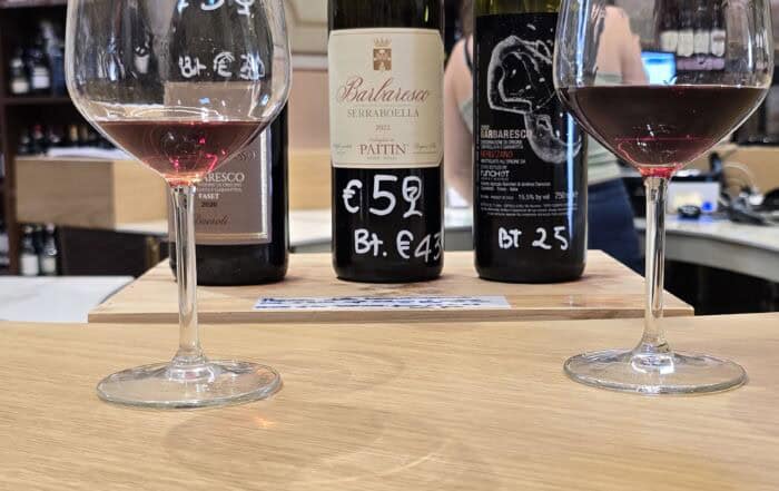 Două pahare de vin roșu alături de trei sticle de vin în interiorul unui spațiu elegant.